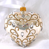 Hjerteformet julekule i perlemorfarge med gulldetaljer og dråpeformede blanke glassteiner. Juletrepynt