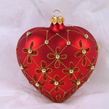 Rødmalt hjerteformet julekule. Dekorert med glitter i blomstermønster og gullperler.