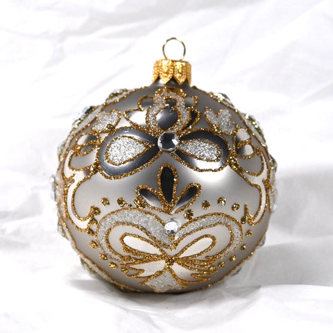 Rund sølvfarget julekule I glass. Dekorert med gull- og sølvglitter og blanke glassteiner. Juletrepynt
