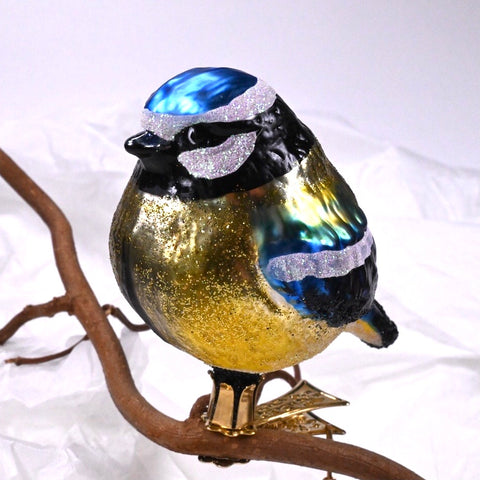 Glassfikur, julekule formet som blåmeis med clip til å feste på grener eller lignende. Glassfigur malt i gull, blå og hvit med gullglitter